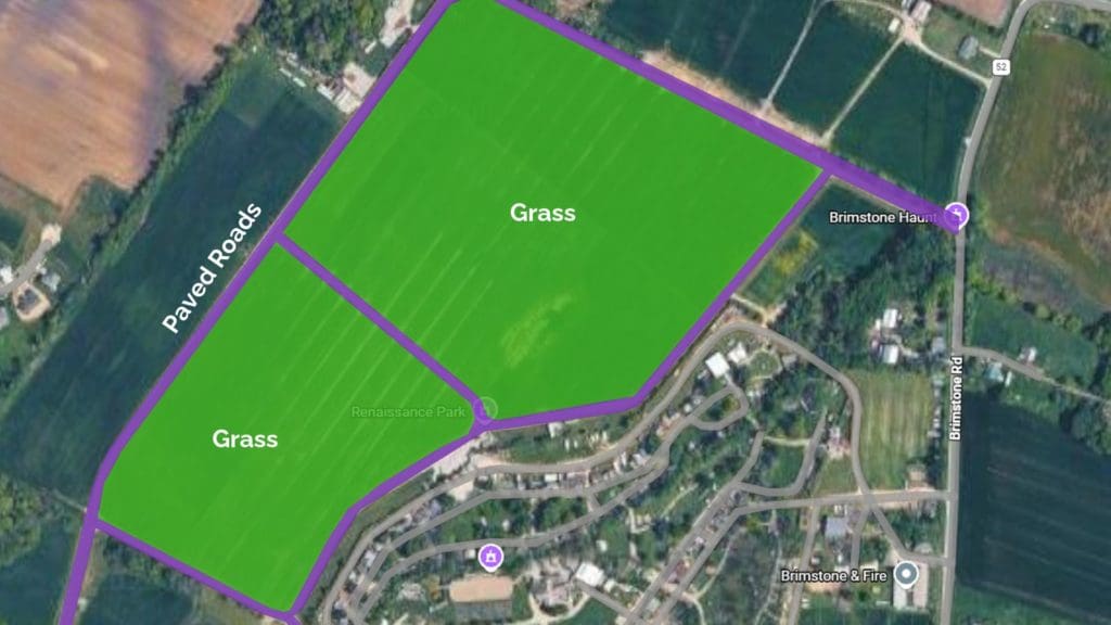 An annotated aerial map from Google Maps showing the parking terrain near Renaissance Park, close to Brimstone Haunt and Brimstone & Fire. Two large areas are filled solid green, labeled "Grass," marking the open lawn sections designated for parking. Purple lines labeled "Paved Roads” showing the access route bordering the grass lots. Nearby roads (Brimstone Rd, Route 52) and surrounding farmland are visible for context, with map pins marking key points of interest near the venue entrances. 